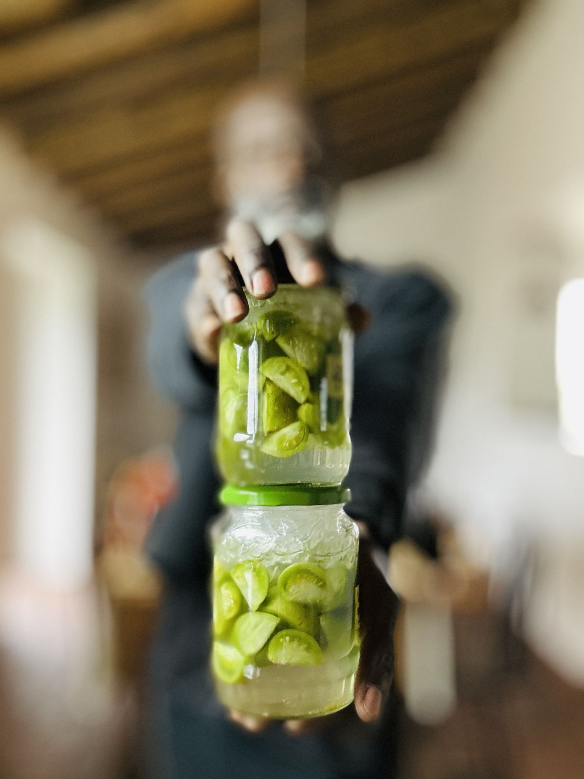 two jars of green tomatoes, held out towards the camera