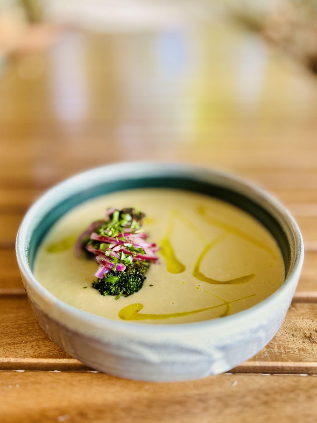 a pale green soup with pickled red onion and charred broccoli in a handmade bowl